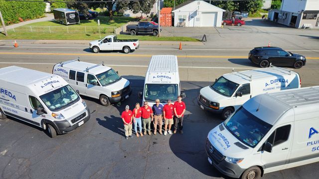 Work trucks and vans parked around a group of workers in red shirts posing outdoors.