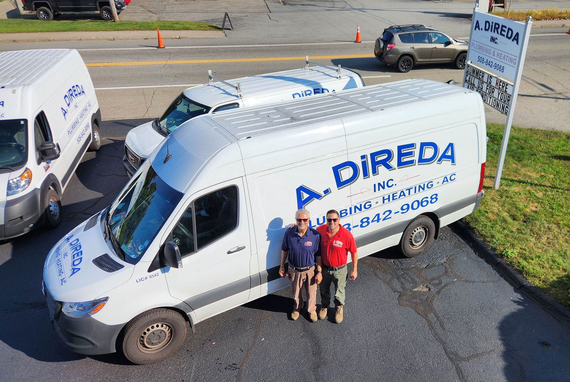 Three people stand beside a white A. Direda work van in a parking lot, viewed from above.