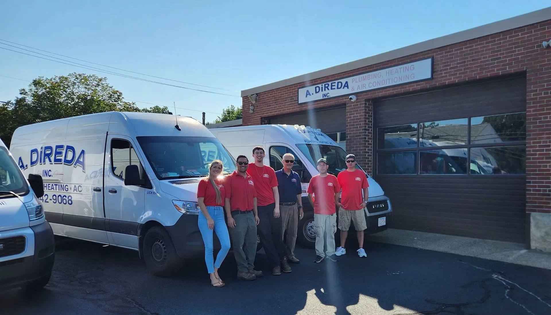 Group posing by white vans outside a brick building on a sunny day