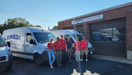 Group posing by white vans outside a brick building on a sunny day