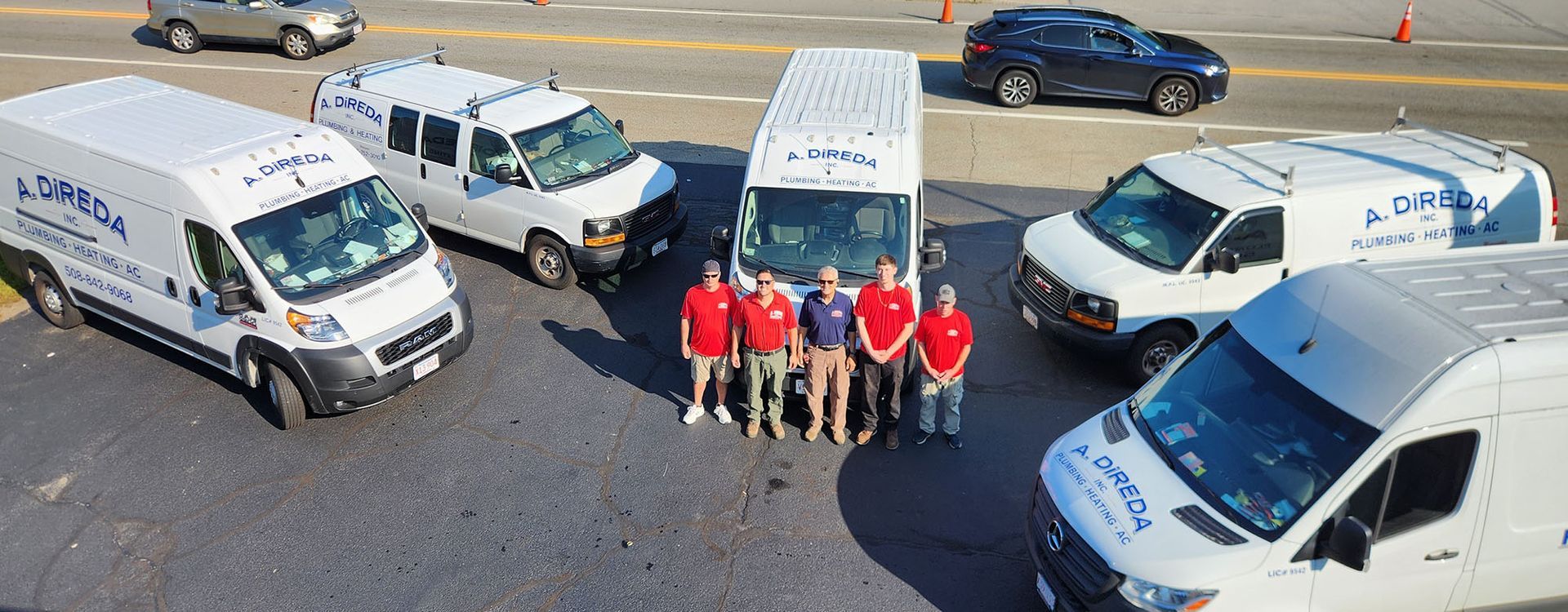 Group in red shirts standing between parked white vans in a lot, with cars in the background.