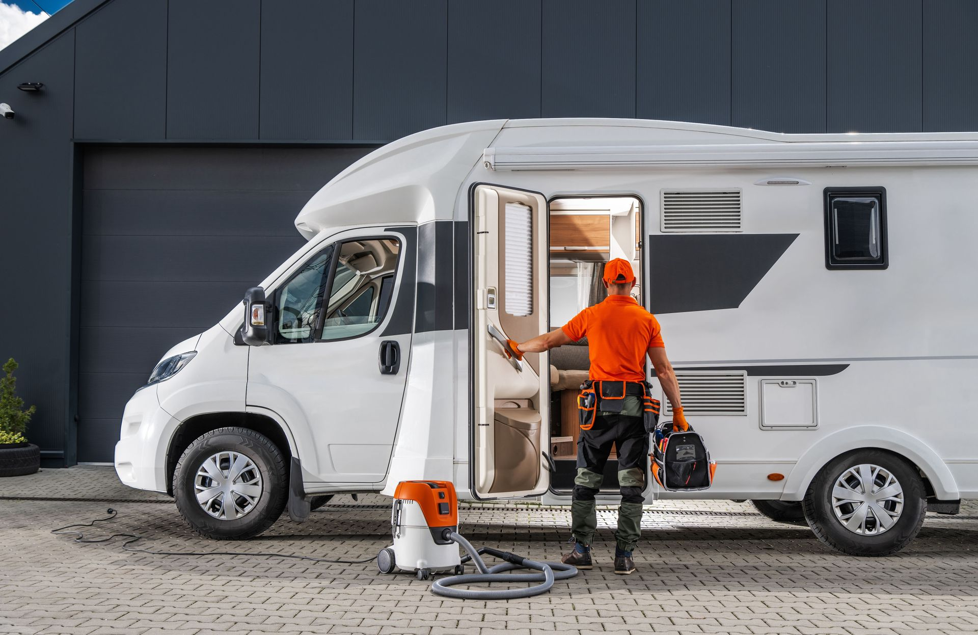 Man in orange outfit with tools near white RV.