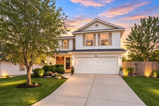 Two-story suburban house with white garage, landscaped front yard, and driveway at sunset