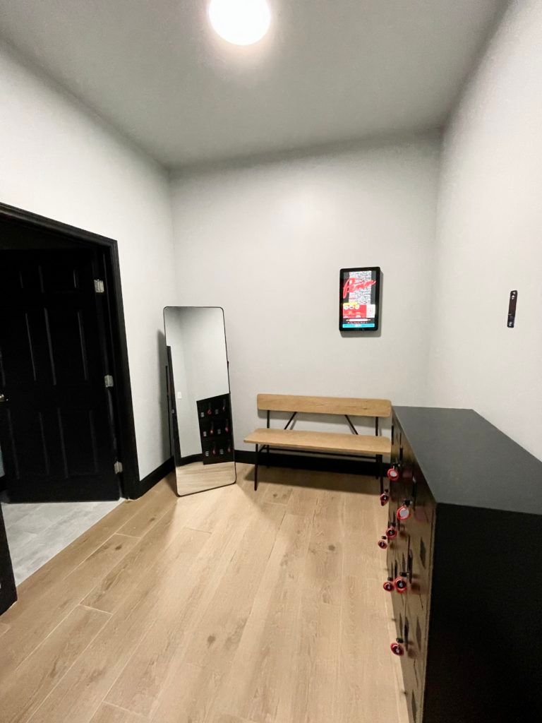 A room with a bench , mirror , lockers and a picture on the wall.