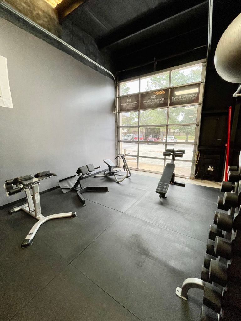 A gym with a lot of exercise equipment and a garage door.