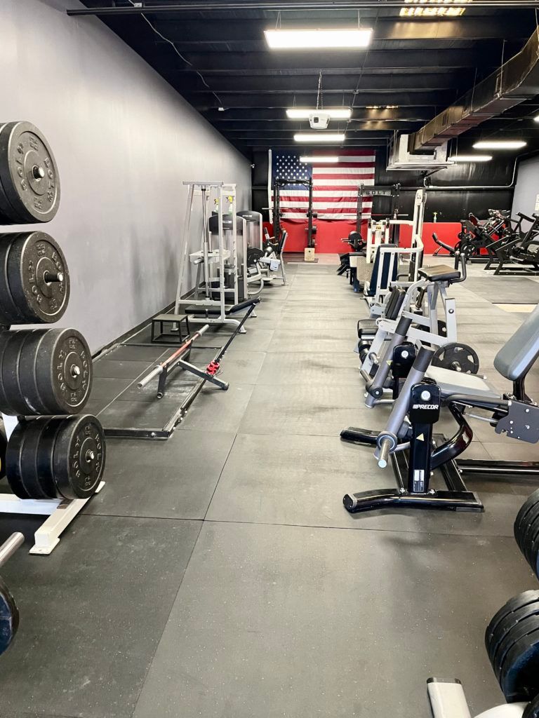 A gym with a lot of equipment and a large american flag on the wall.