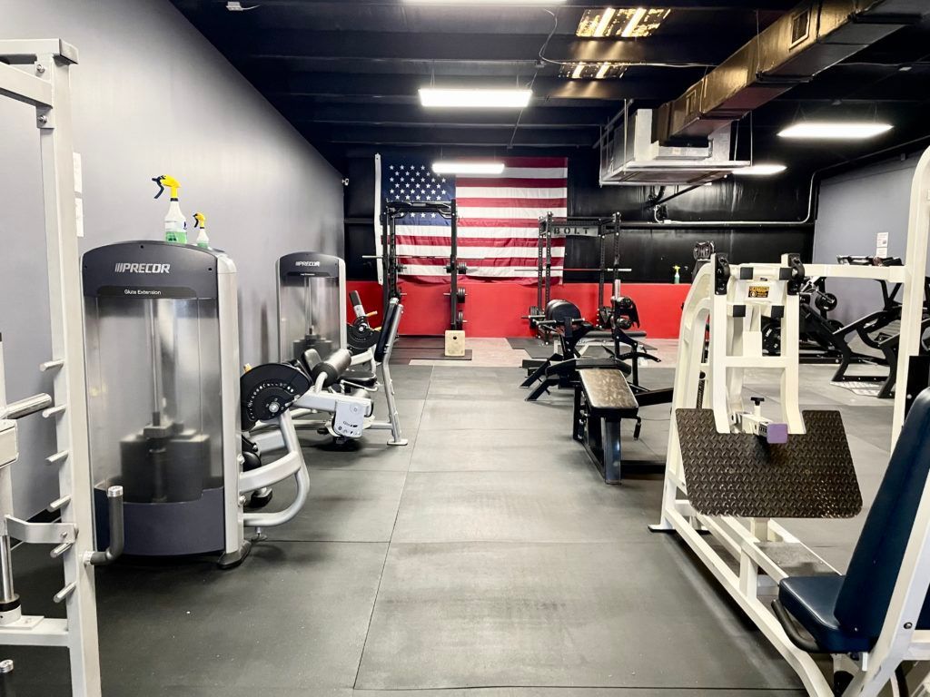 A gym filled with lots of exercise equipment and an american flag on the wall.