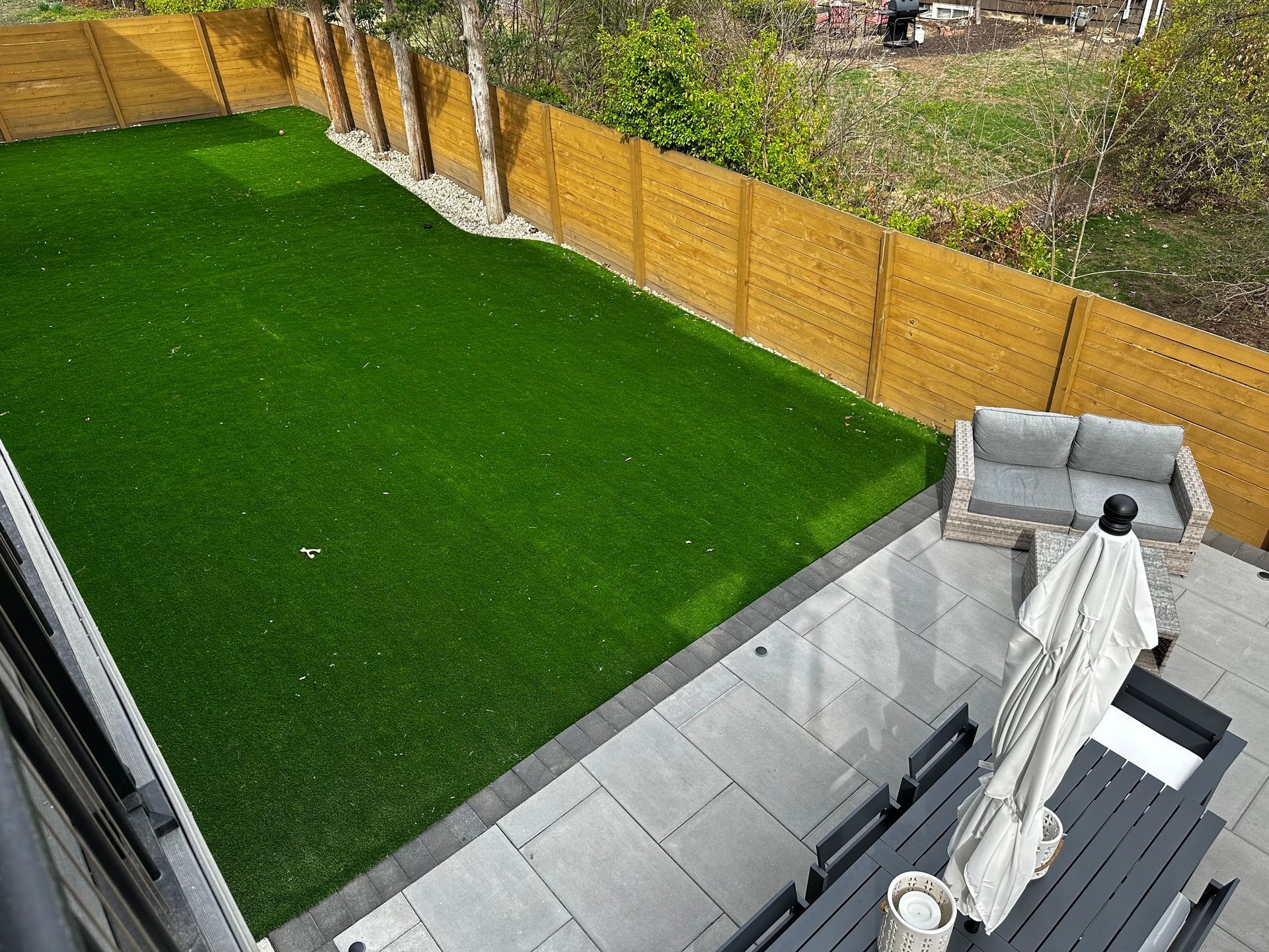 Backyard with bright green lawn, wooden fence, and a patio with covered furniture.