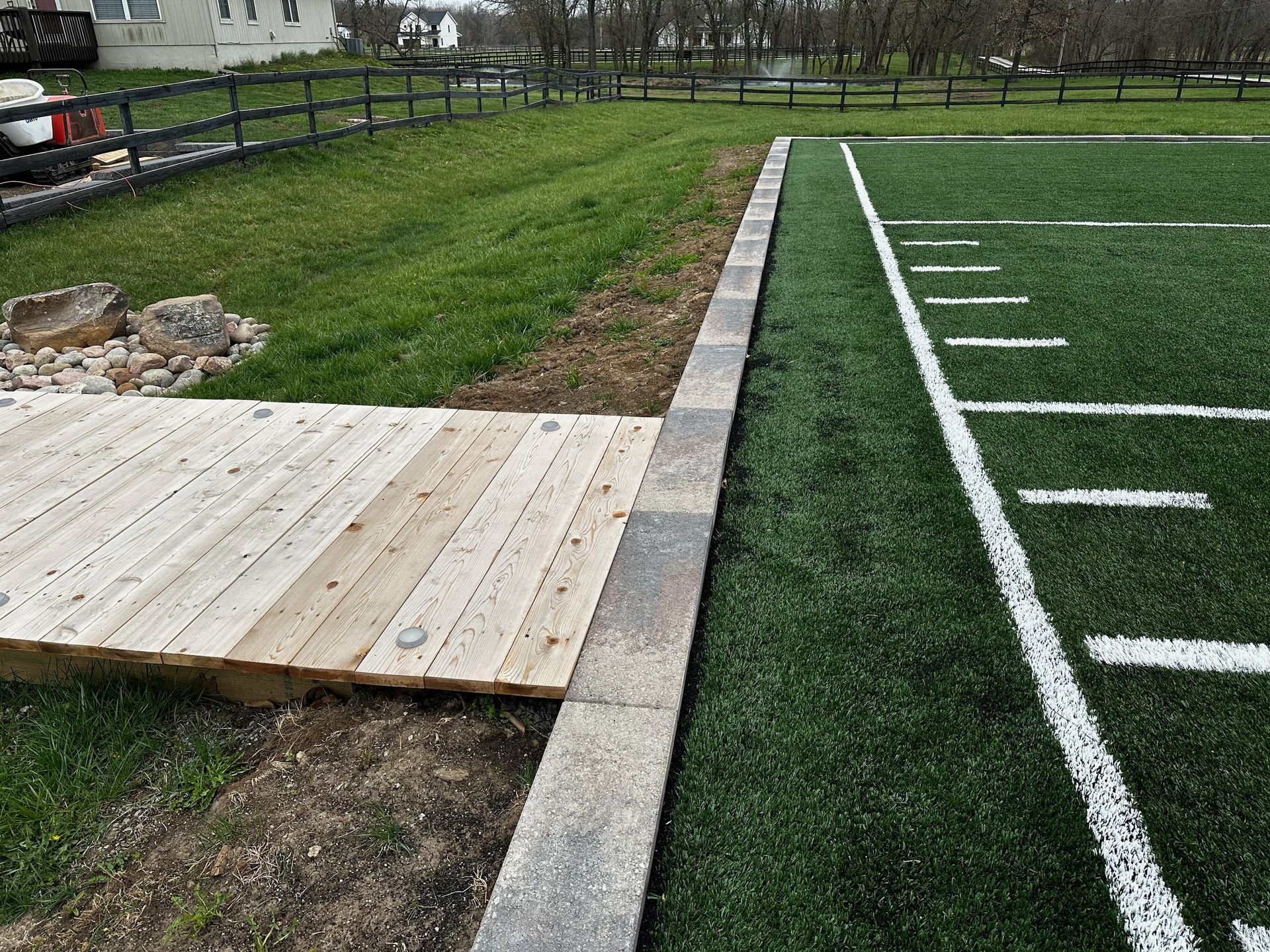 Wooden ramp beside a turf sports field with white yard lines and a grassy area beyond.