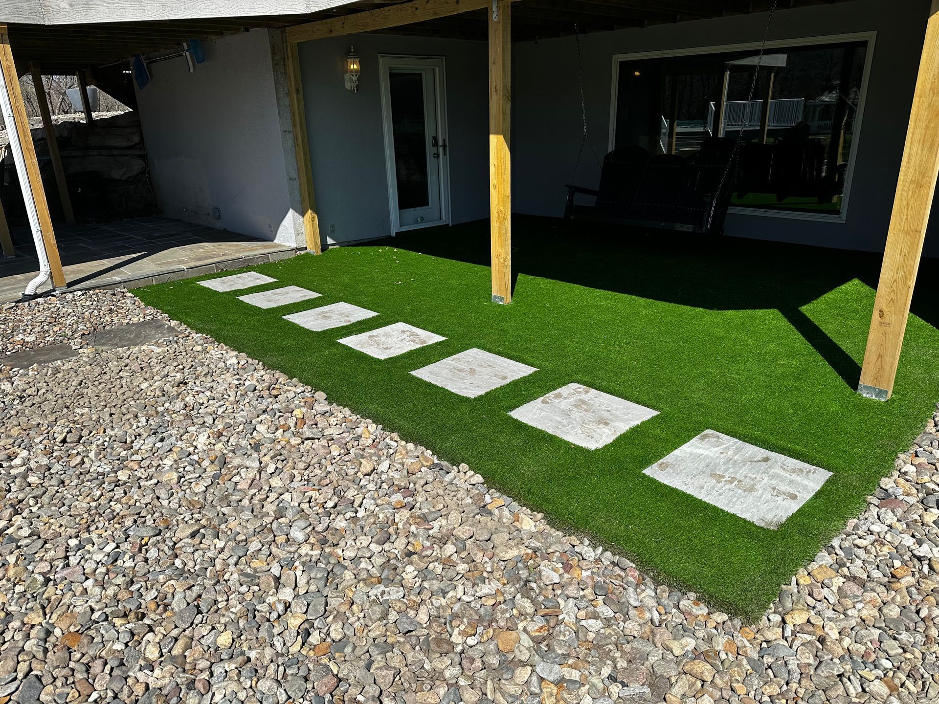 Gravel walkway beside a building, with white stepping stones across bright green turf under a covered patio