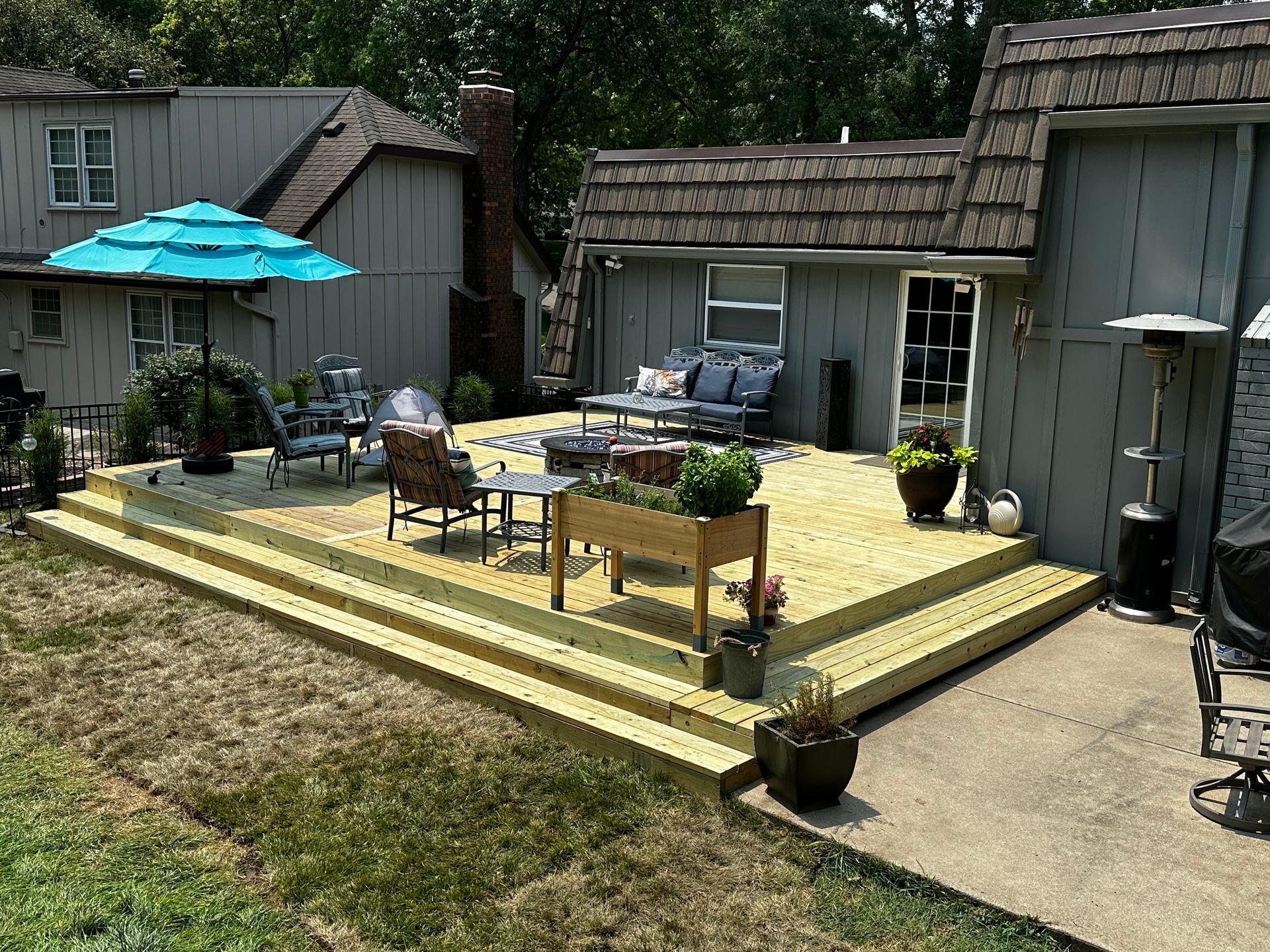 Backyard deck with patio table, umbrella, chairs, and potted plants beside a shed and garage.
