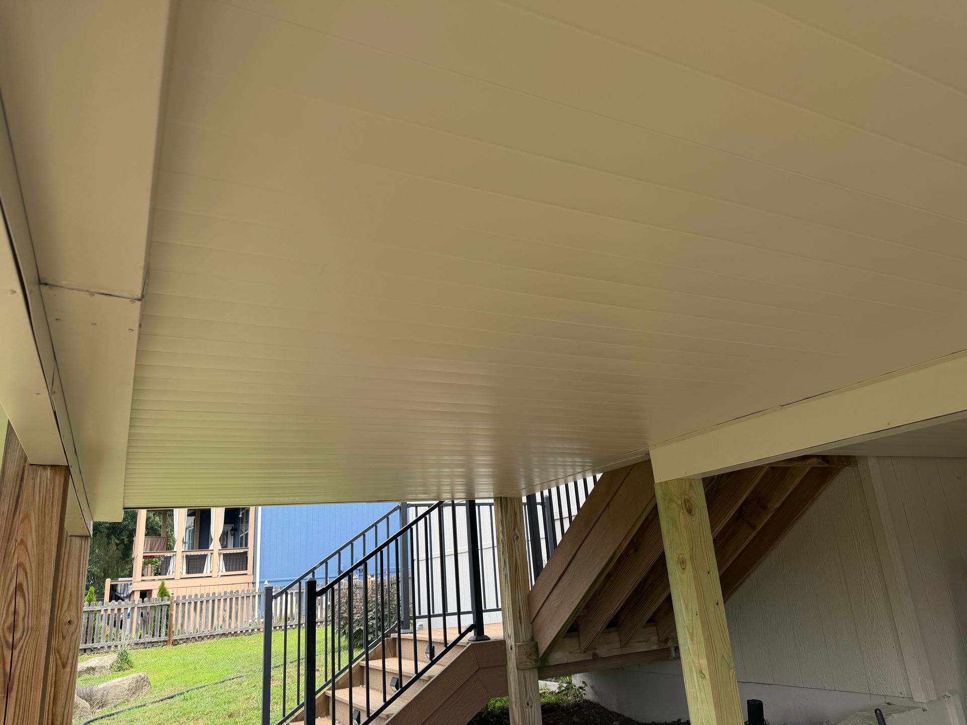 Under-deck area with white ceiling, support posts, stairs, and a backyard view beyond the railing