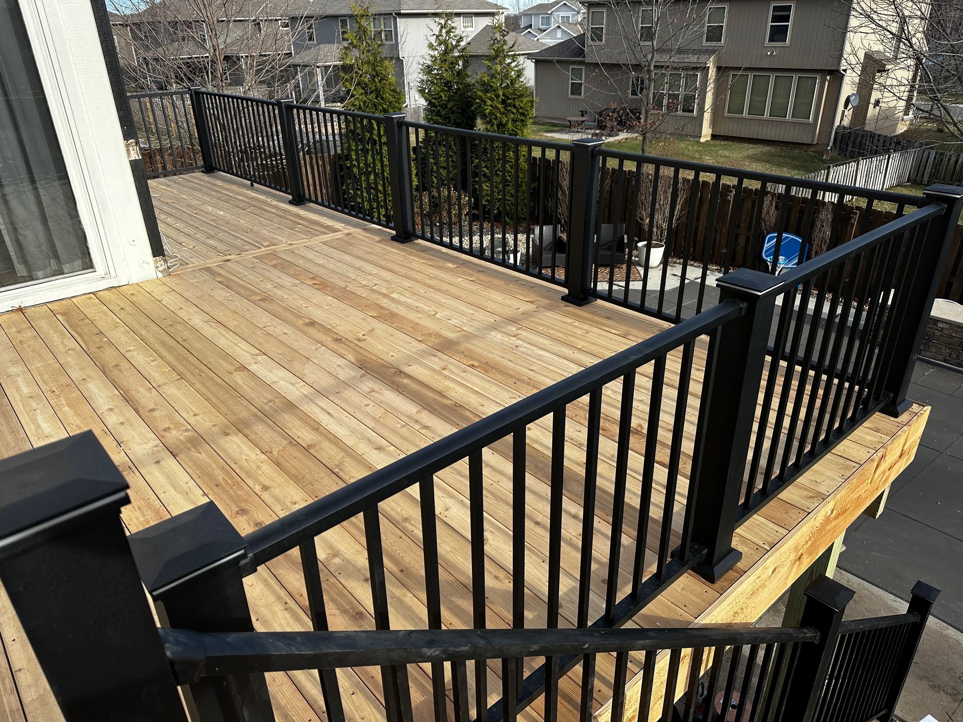 Wooden deck with black metal railing and stairs overlooking neighboring houses and trees