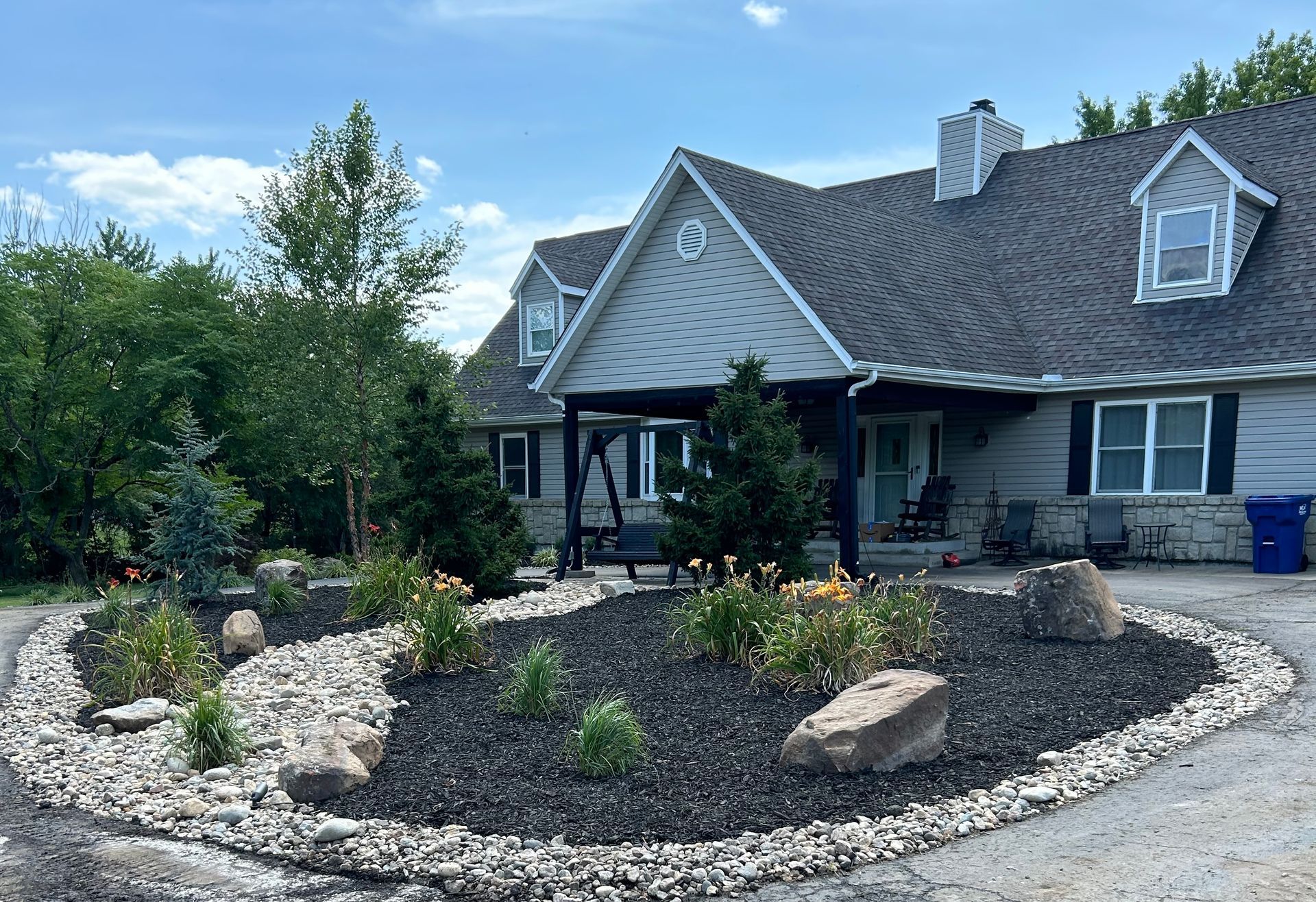 Landscaped front yard with rock garden in front of a gray house under a blue sky