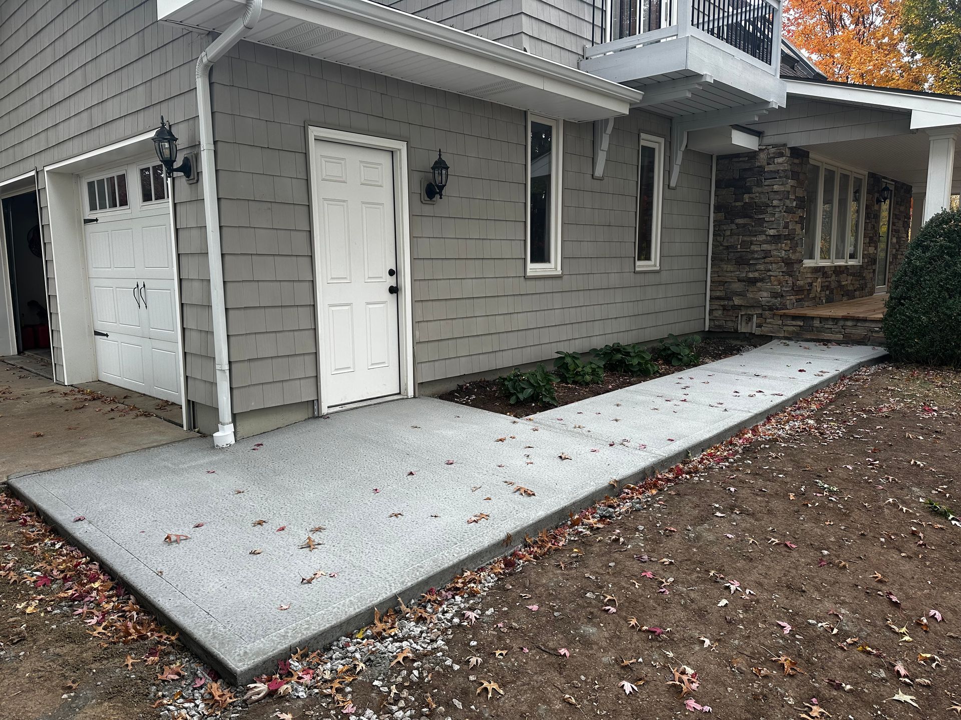 Gray house exterior with a white front door, concrete walkway, and fallen autumn leaves