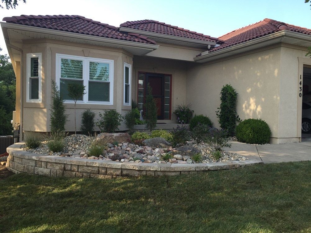 Beige stucco house with red tile roof, landscaped yard with stone retaining wall.
