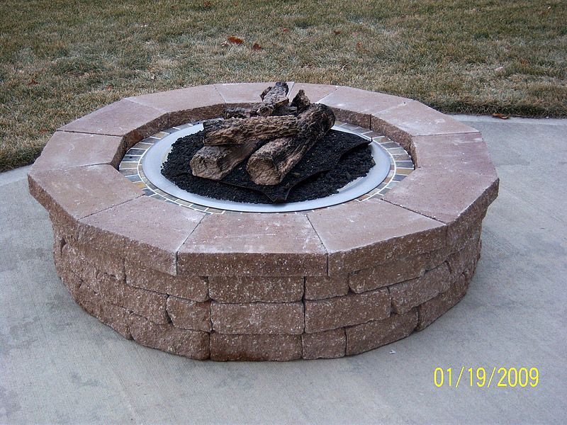 Fire pit made of brick with logs and black stones on a patio.
