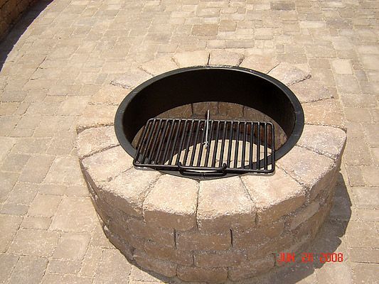 Stone fire pit with metal grill insert on a paved patio.