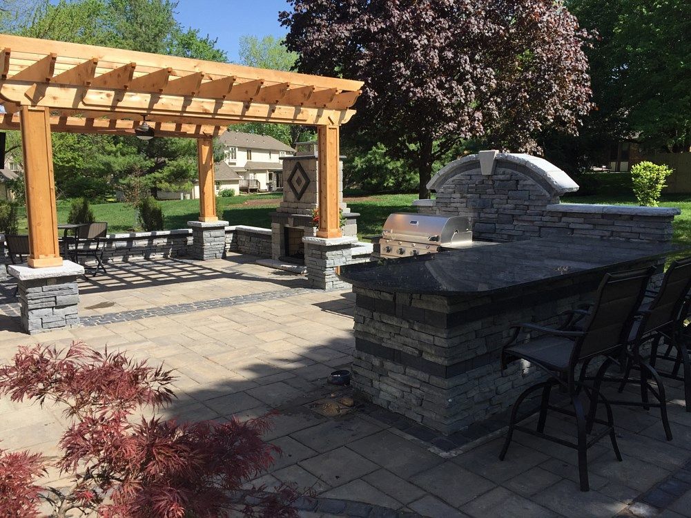 Outdoor patio with pergola, built-in grill, and bar seating. Features stone work and a dark granite countertop.
