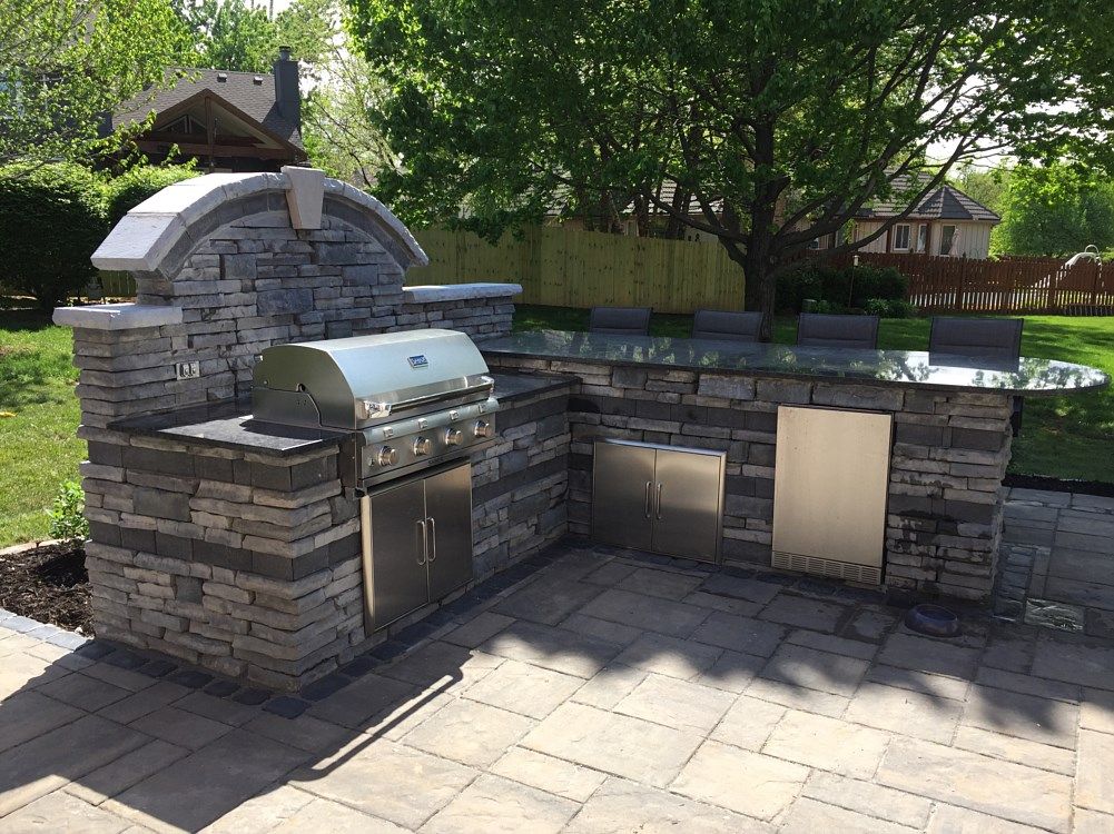 Outdoor stone kitchen with grill, oven, cabinets, and countertop bar.