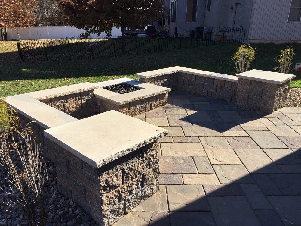 Stone patio with built-in fire pit and seating walls in a backyard setting.