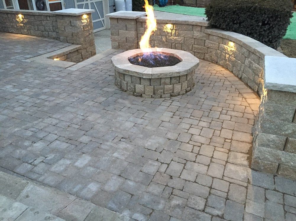 Stone patio with fire pit, surrounded by low walls with built-in lights.
