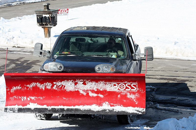 Black truck with red snowplow clearing snow on a sunny day.