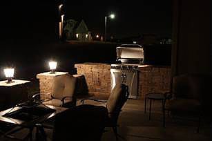 Patio with grill, seating, and lanterns lit at night.