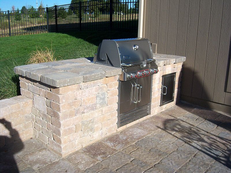 Outdoor brick barbecue grill island with stainless steel grill and side door.
