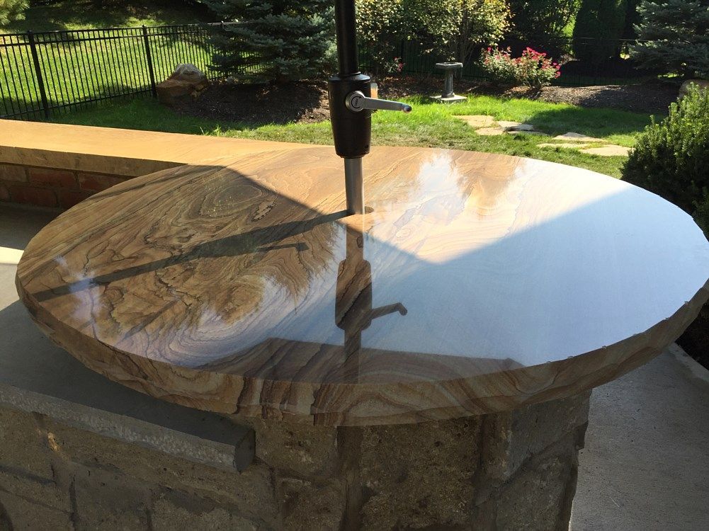 Round stone patio table with umbrella in a sunny outdoor setting.