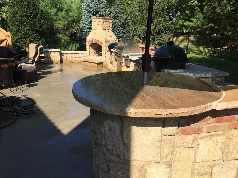 Outdoor kitchen with stone and brick features, including a grill, fireplace, and bar.