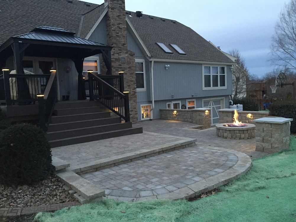Backyard patio with fire pit, steps, and deck at dusk.