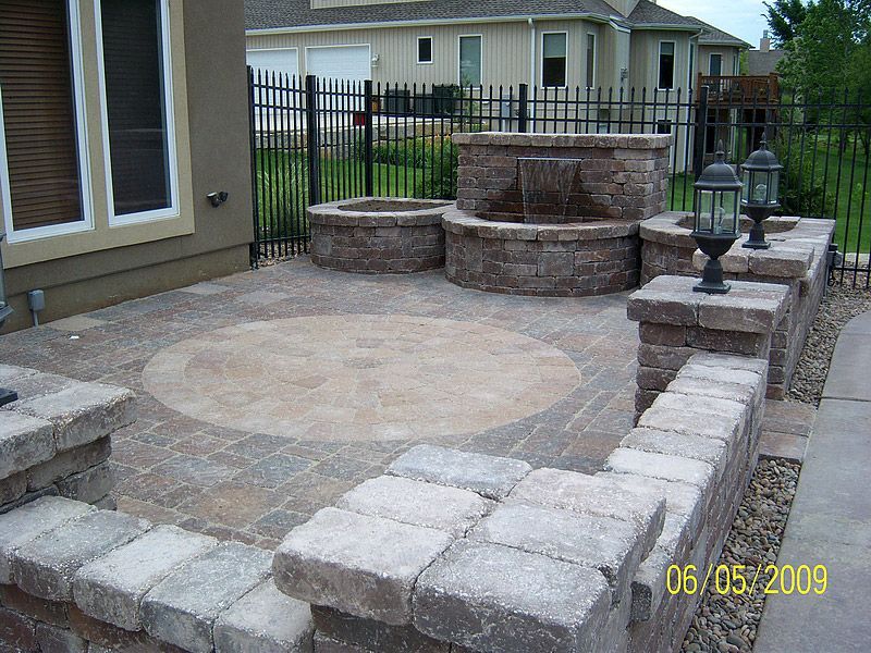 Stone patio with water feature, walls, and iron fence in a residential backyard.