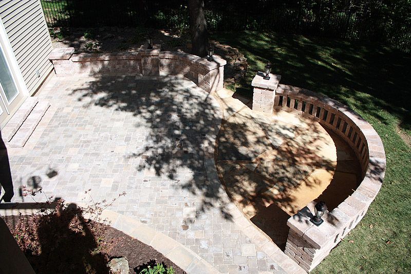 Brick patio with curved retaining wall and tree shadow.