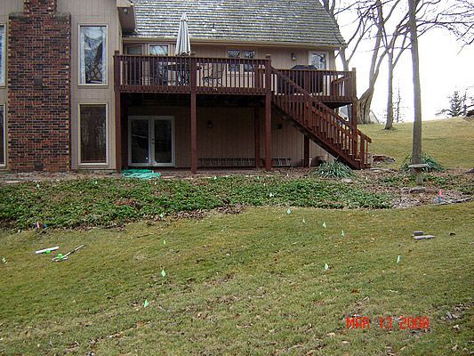 Brown wooden deck with stairs attached to a beige house, overlooking a grassy hill.