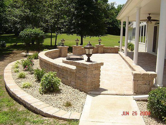 Stone patio with a low wall, garden, and a house porch on a sunny day.