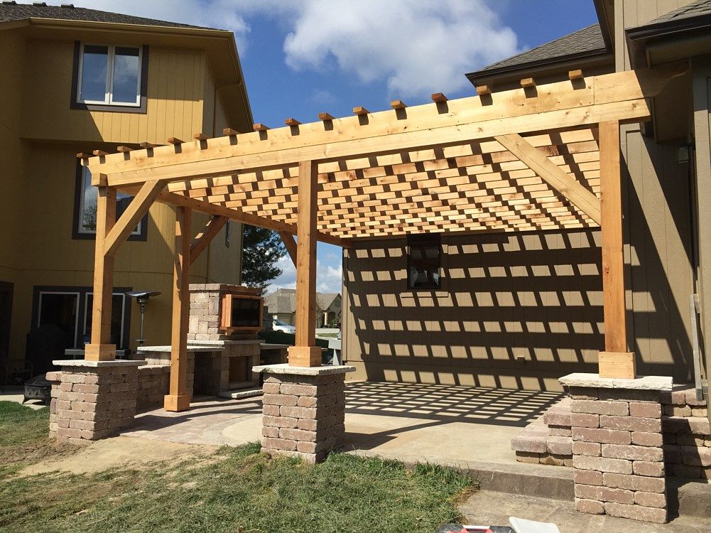 Wooden pergola with brick pillars casting a grid shadow on patio.