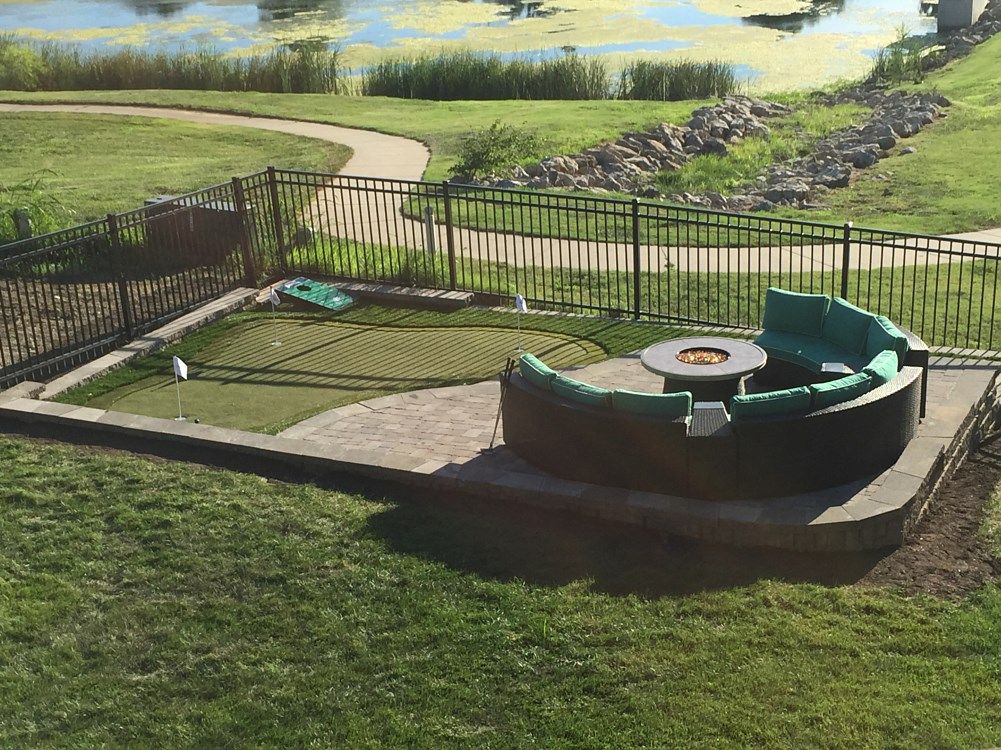 Outdoor seating area with fire pit, putting green, and pond in background.