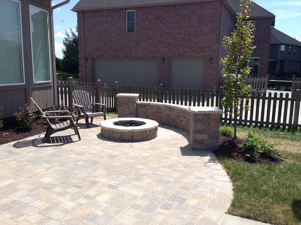 Patio with fire pit, seating, and curved brick wall in front of a house.