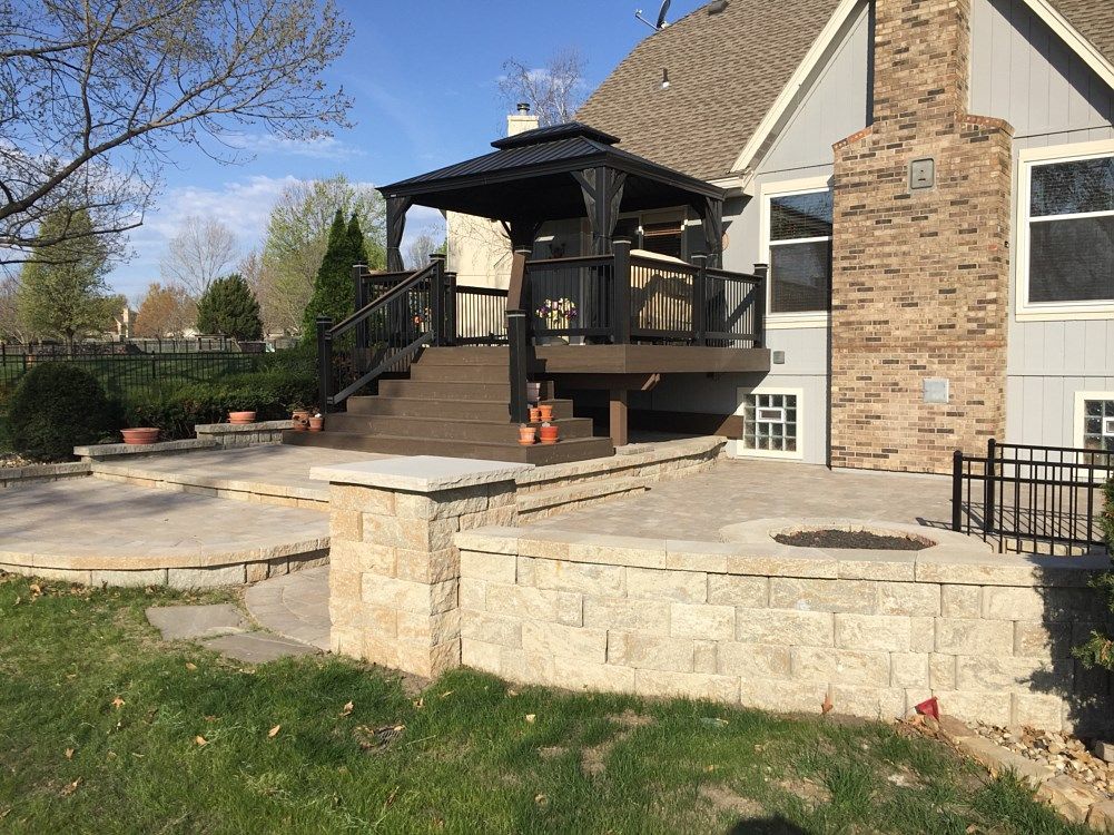 A tiered backyard patio with a deck, gazebo, and stone retaining walls.