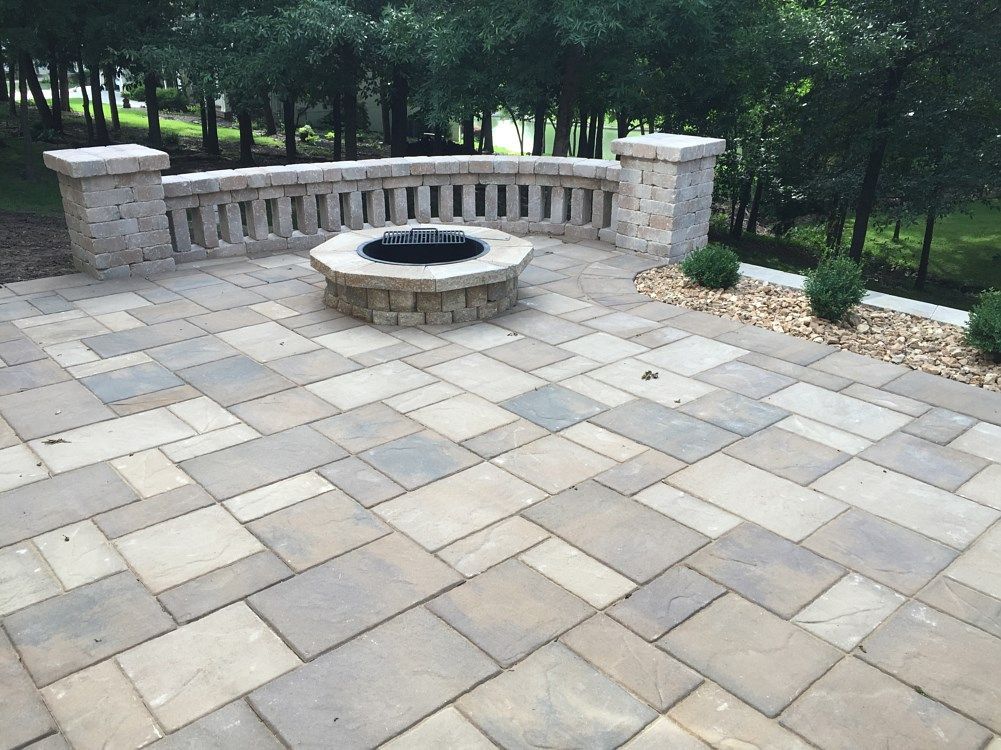 Stone patio with built-in fire pit and decorative stone wall. Trees in the background.