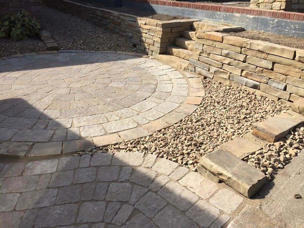 Stone patio with curved brick detail, gravel, and tiered retaining wall.