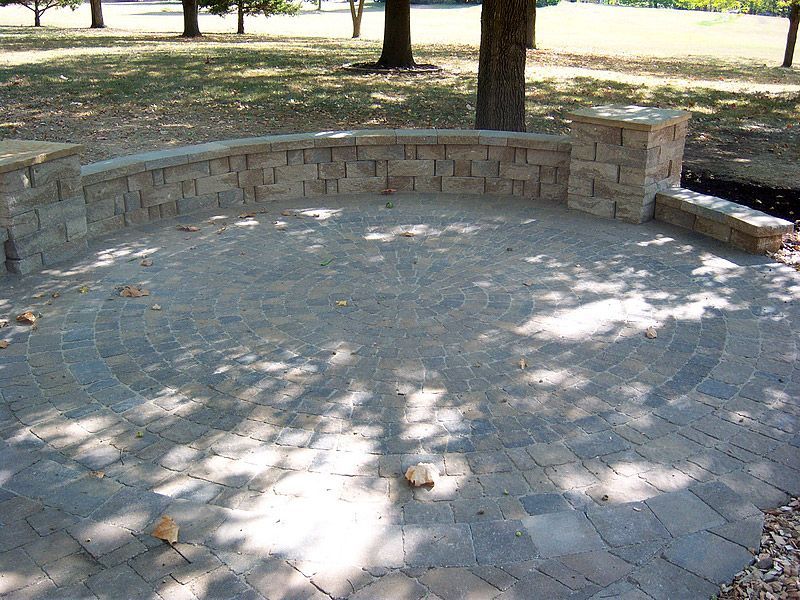 Stone patio with curved brick wall, in a park setting.