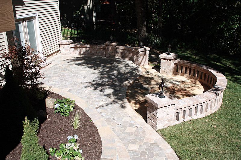 Brick patio with curved retaining wall and walkway, surrounded by grass and landscaping.