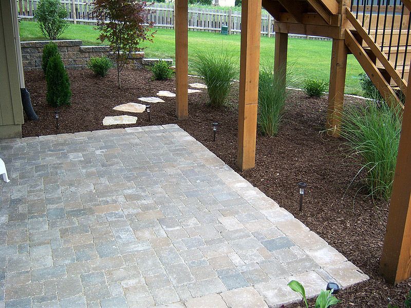 Patio with stone pavers and mulch garden beneath wooden deck with stepping stones.