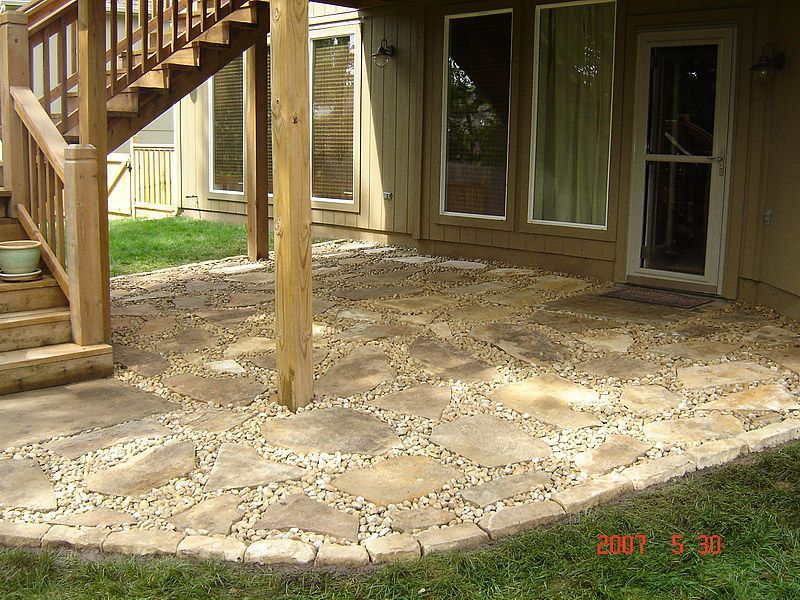 Stone patio with wooden staircase, beige siding, and grass lawn.