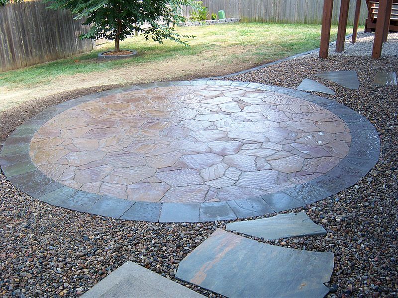 Circular stone patio surrounded by gravel, with stepping stones and a backyard setting.
