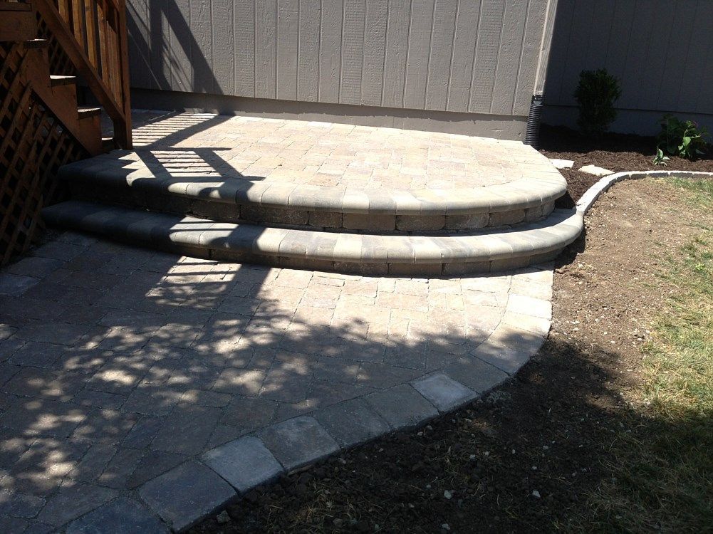 Stone steps and patio leading to a wooden deck, bordered by grass and mulch.