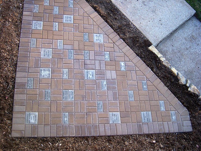 Brown brick patio with embedded silver tiles, edged in a dark border and adjacent to a concrete slab.