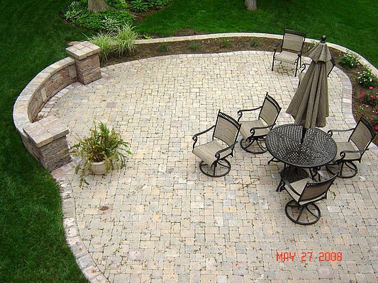 Brick patio with round table and chairs, surrounded by grass and a low wall.